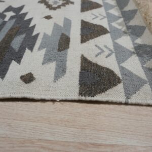 Geometric flat weave rug in neutral gray, brown, and cream colors on light wood floor.