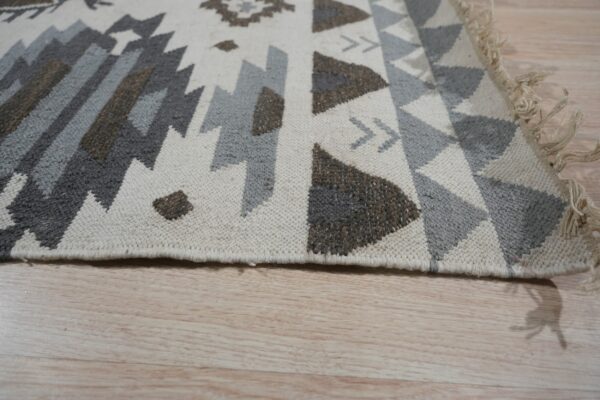 Geometric flat weave rug in neutral gray, brown, and cream colors on light wood floor.