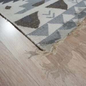 Low-pile geometric rug in cream, light gray, and brown on glossy light wood planks.