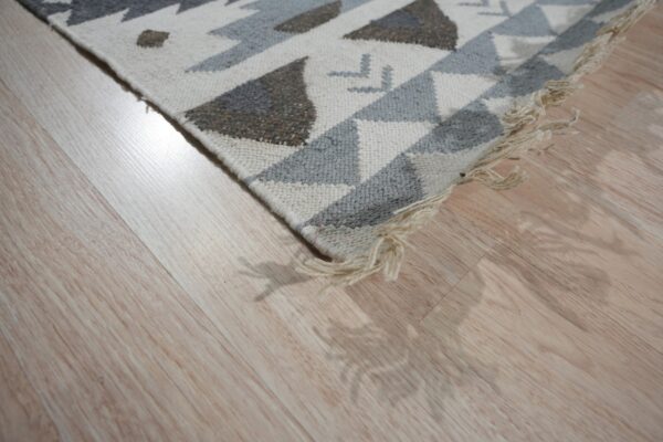 Low-pile geometric rug in cream, light gray, and brown on glossy light wood planks.