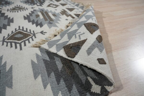 Close-up of a white, gray, and brown geometric rug folded over on pale wood planks.