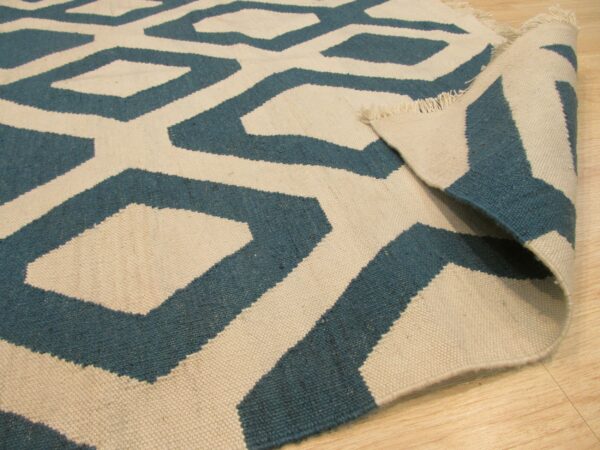 Teal and cream flat-weave rug featuring a geometric pattern is displayed folded on light wood flooring.