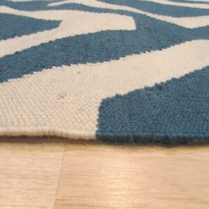 Low pile rug edge showing blue and cream geometric pattern on light blonde hardwood floors.