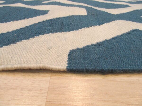 Low pile rug edge showing blue and cream geometric pattern on light blonde hardwood floors.