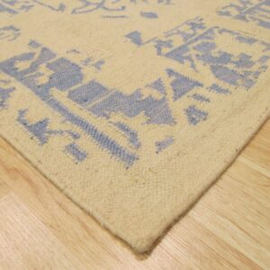 A cream and blue patterned low-pile rug corner rests on glossy light wood planks.