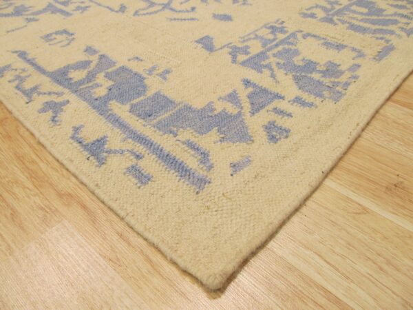 A cream and blue patterned low-pile rug corner rests on glossy light wood planks.