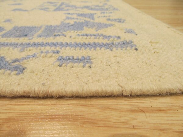 Extreme close-up of a low pile cream rug featuring a textured light blue loop pattern on wood flooring.