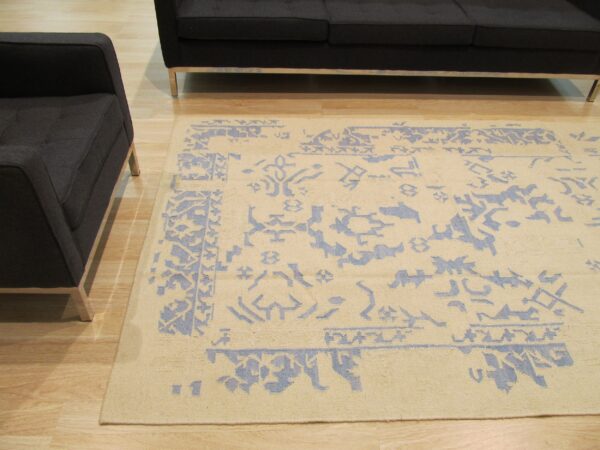 Light beige rug with faded blue traditional patterns sits between a dark sofa and armchair on wood floor.