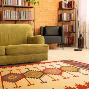 Flat-woven geometric rug in cream, red, and dark tones highlights a room with a green sofa and brick wall.