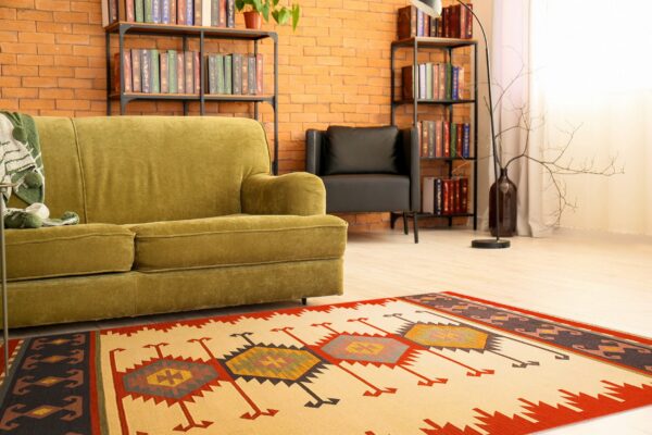Flat-woven geometric rug in cream, red, and dark tones highlights a room with a green sofa and brick wall.