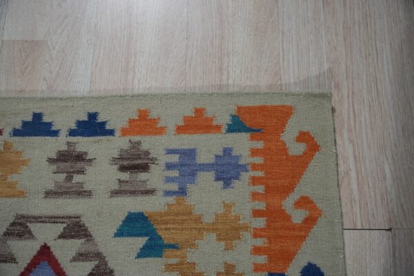Beige flatweave rug with orange, blue, and brown geometric patterns on pale wood floor.