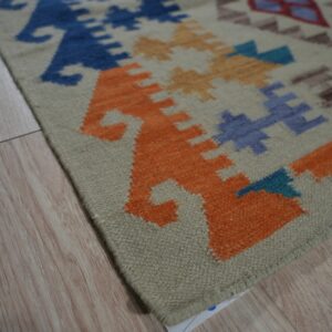 Low-pile rug with bright orange, blue, and tan geometric motifs on light wood plank floor.