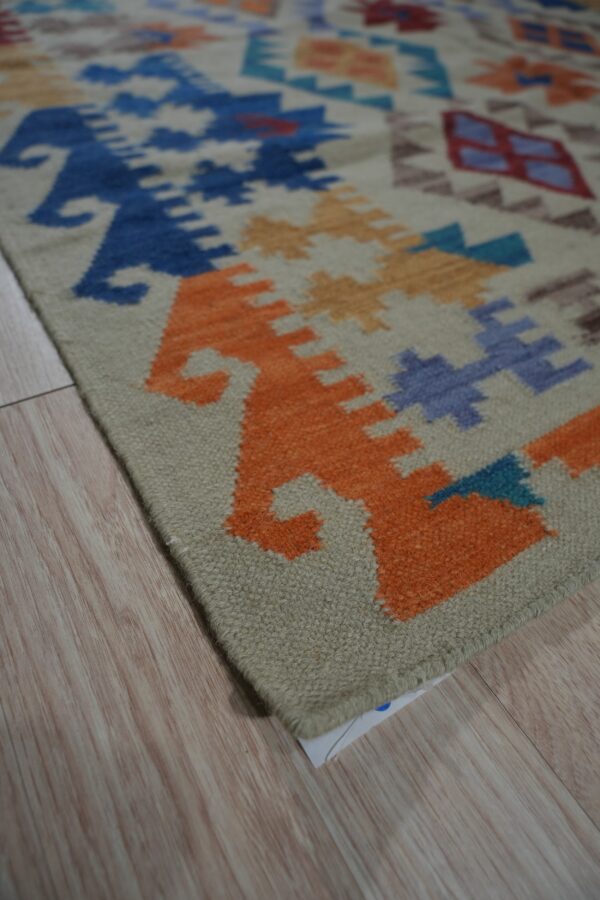 Low-pile rug with bright orange, blue, and tan geometric motifs on light wood plank floor.