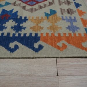 Geometric rug corner featuring blue, orange, and tan motifs resting on pale wood plank flooring.