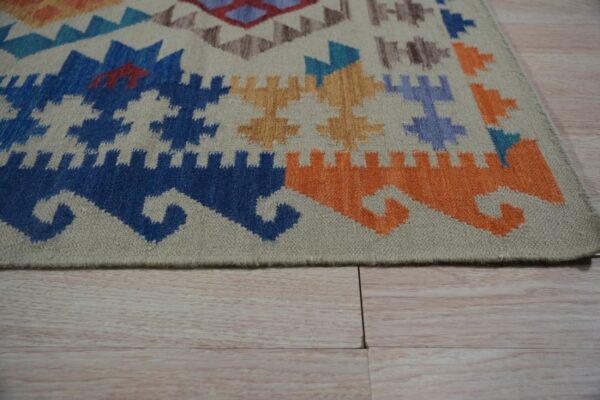 Geometric rug corner featuring blue, orange, and tan motifs resting on pale wood plank flooring.