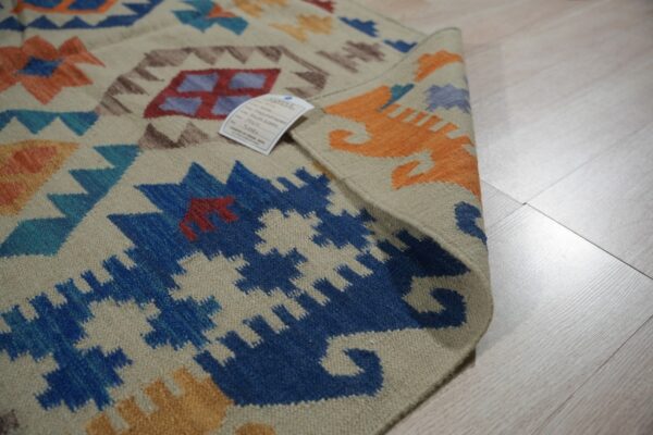 Close-up of a beige rug with bright blue, orange, and red geometric patterns on light wood flooring.