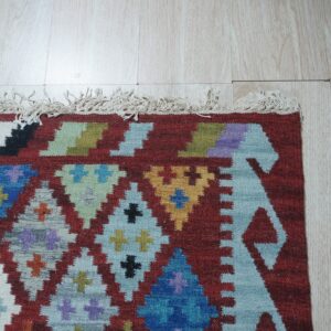 Multicolor flatweave rug with geometric diamonds and fringe against light wood plank flooring.