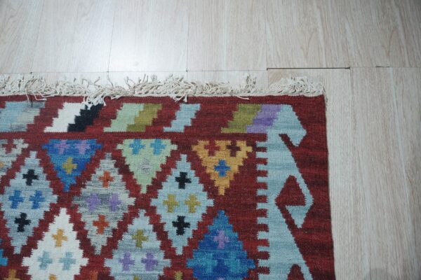 Multicolor flatweave rug with geometric diamonds and fringe against light wood plank flooring.