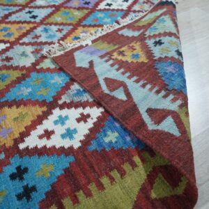 Geometric, multicolored flatwoven rug with stepped diamonds and fringe rests on a light wooden floor.