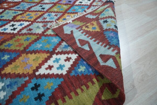 Geometric, multicolored flatwoven rug with stepped diamonds and fringe rests on a light wooden floor.