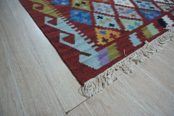 A colorful geometric flatweave rug with tassels rests on light wood flooring.