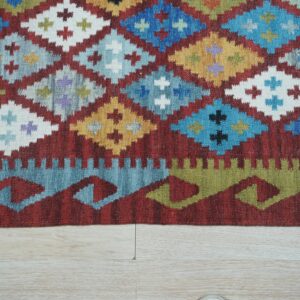 Close-up of a flatwoven rug displaying colorful diamonds and sawtooth borders against pale wood planks.