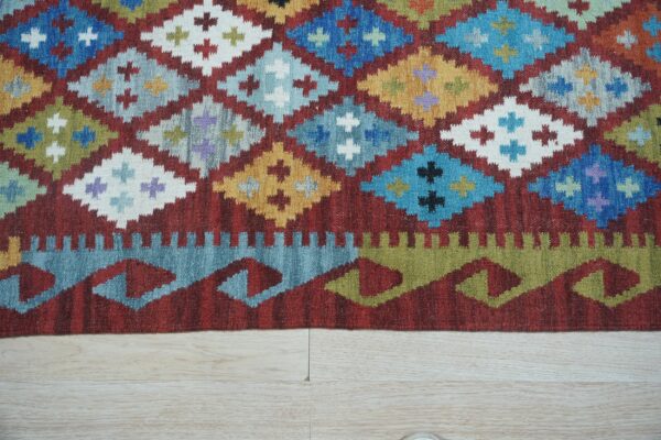 Close-up of a flatwoven rug displaying colorful diamonds and sawtooth borders against pale wood planks.