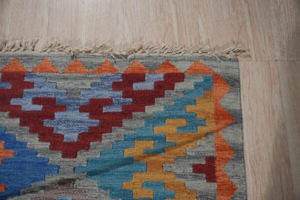 Stepped geometric pattern rug in gray, red, blue, and yellow on light wood floor with short fringe.