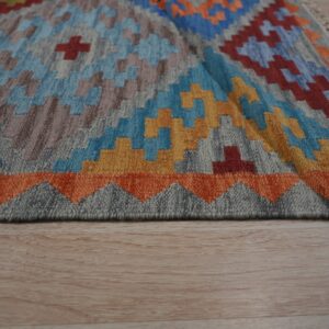 Colorful flatweave rug with geometric blue, orange, yellow, and gray patterns on light wood flooring.