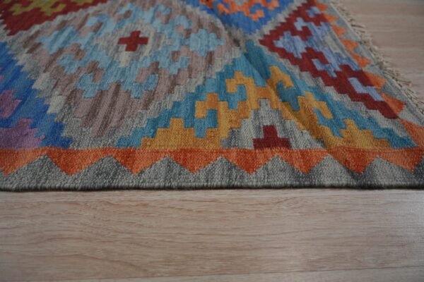 Colorful flatweave rug with geometric blue, orange, yellow, and gray patterns on light wood flooring.