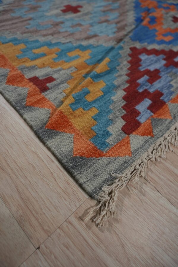 Close-up view of a flat-woven rug with multicolor geometric patterns and fringe on light wood flooring.