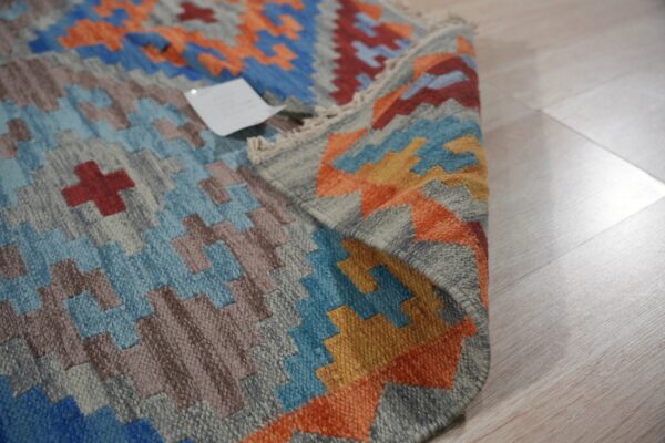 Geometric flatweave rug featuring stepped patterns in blue, orange, gray, and brown on light plank flooring.