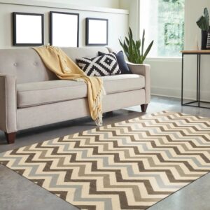 A brown, cream, and blue zigzag rug sits under a beige sofa on a polished concrete floor.