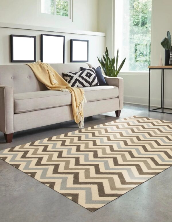 A brown, cream, and blue zigzag rug sits under a beige sofa on a polished concrete floor.