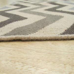Low-pile chevron rug in cream, gray, and charcoal rests on light colored wood flooring.