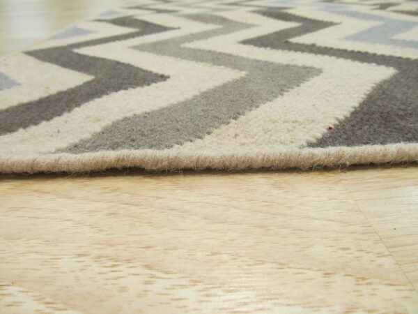 Low-pile chevron rug in cream, gray, and charcoal rests on light colored wood flooring.