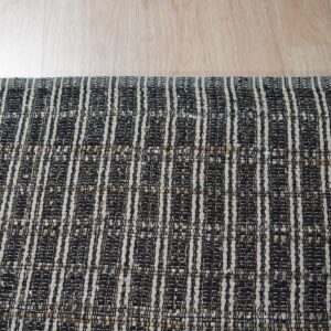 Black and light tan woven rug with vertical stripe patterns covering light wood floor.