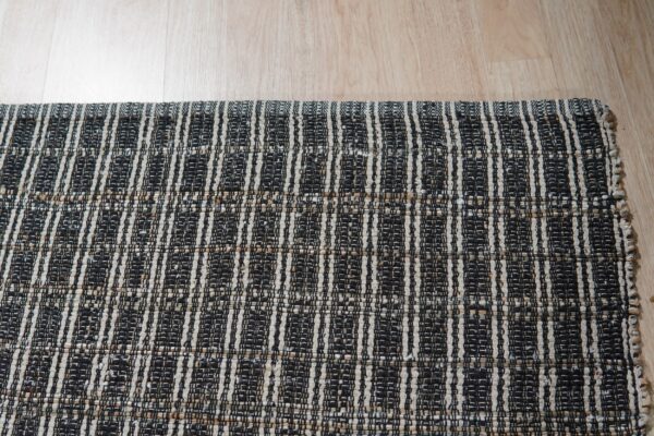 Black and light tan woven rug with vertical stripe patterns covering light wood floor.