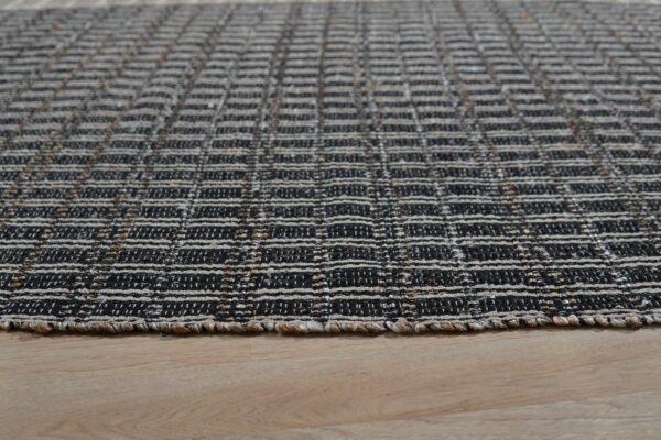 Black and off-white flatweave rug with a horizontal textured grid pattern resting on light hardwood floors.
