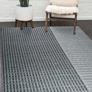 Black and white geometric rug sits on dark wood flooring near a white brick wall and fur chair.