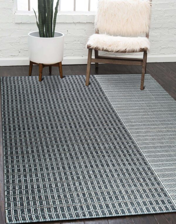 Black and white geometric rug sits on dark wood flooring near a white brick wall and fur chair.