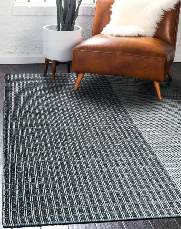 Black and white striped rug with a diagonal color-block pattern beneath a brown leather chair on dark wood flooring.