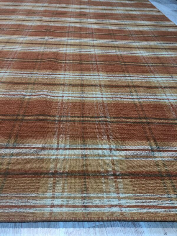 A rust and tan plaid rug with a flat texture sits on light plank flooring.