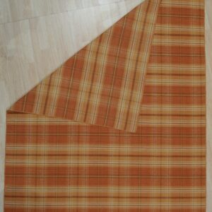 Orange and tan plaid rug displayed on light wood flooring with one corner folded back.