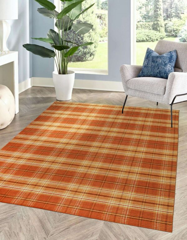 Low profile orange plaid rug placed on light wood floors beside a gray armchair and a large plant.