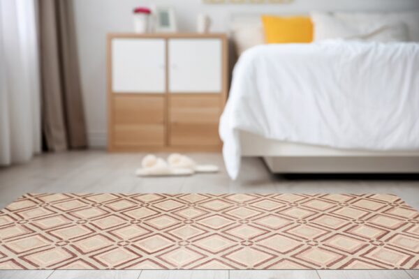 A low profile rug with a brown and tan geometric diamond pattern sits on light flooring in a bright bedroom.