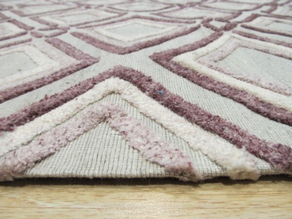 Close-up shows a light gray rug with raised loop pile texture in white and mauve geometric patterns on wood flooring.