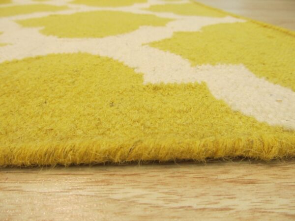 Low angle of a thick, shaggy, yellow and off-white patterned rug edge on wood planks.