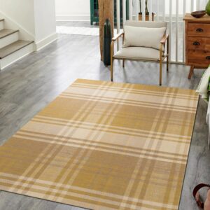 A gold and cream plaid rug rests on gray wood flooring near a white staircase and arm chair.