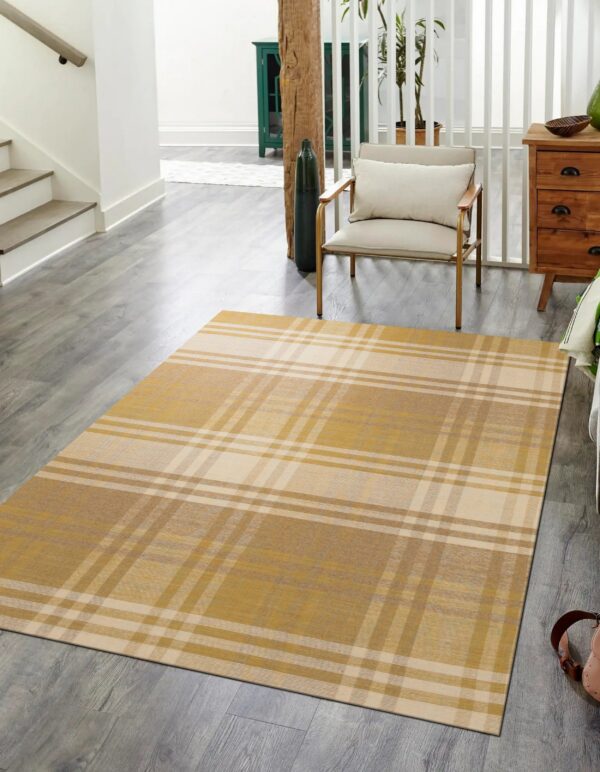 A gold and cream plaid rug rests on gray wood flooring near a white staircase and arm chair.